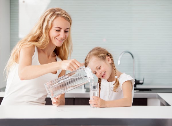 Child with mother drinking water from glass. Happy family at home in kitchen